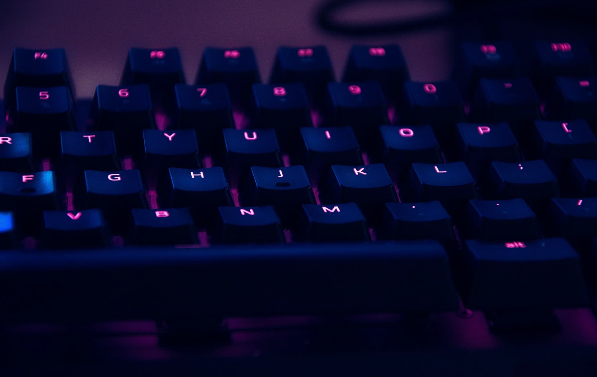 Close-up of a dark mechanical keyboard with keys backlit in pink and blue light