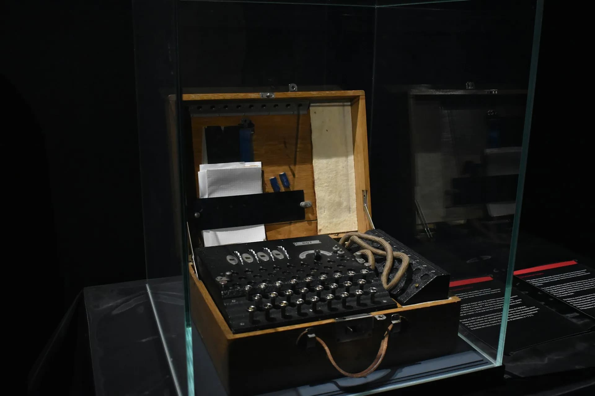 Enigma cipher machine in its open wooden case, displayed inside a glass museum vitrine