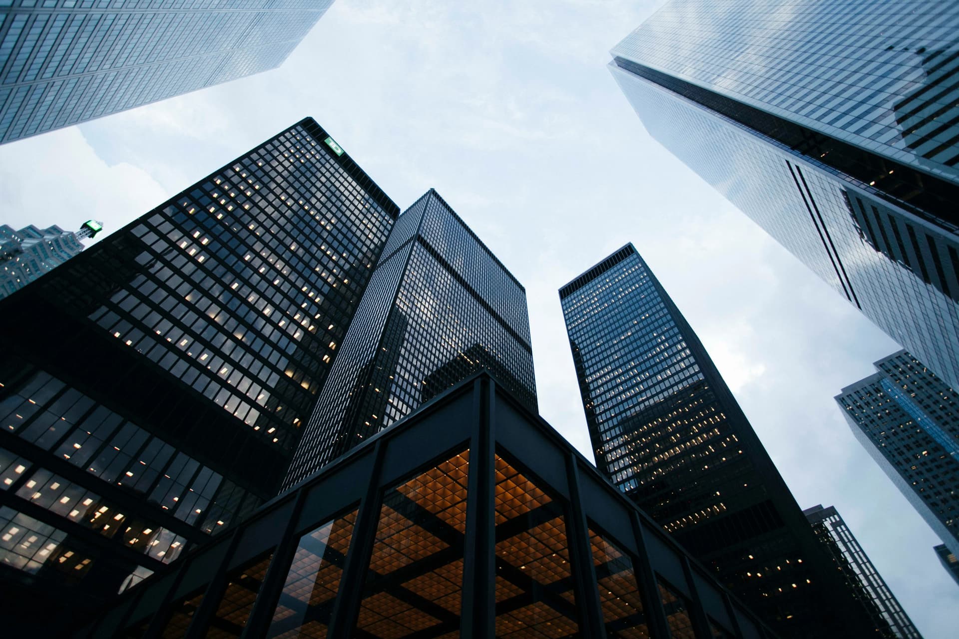 Upward view of dark glass office towers with lit windows against an overcast sky