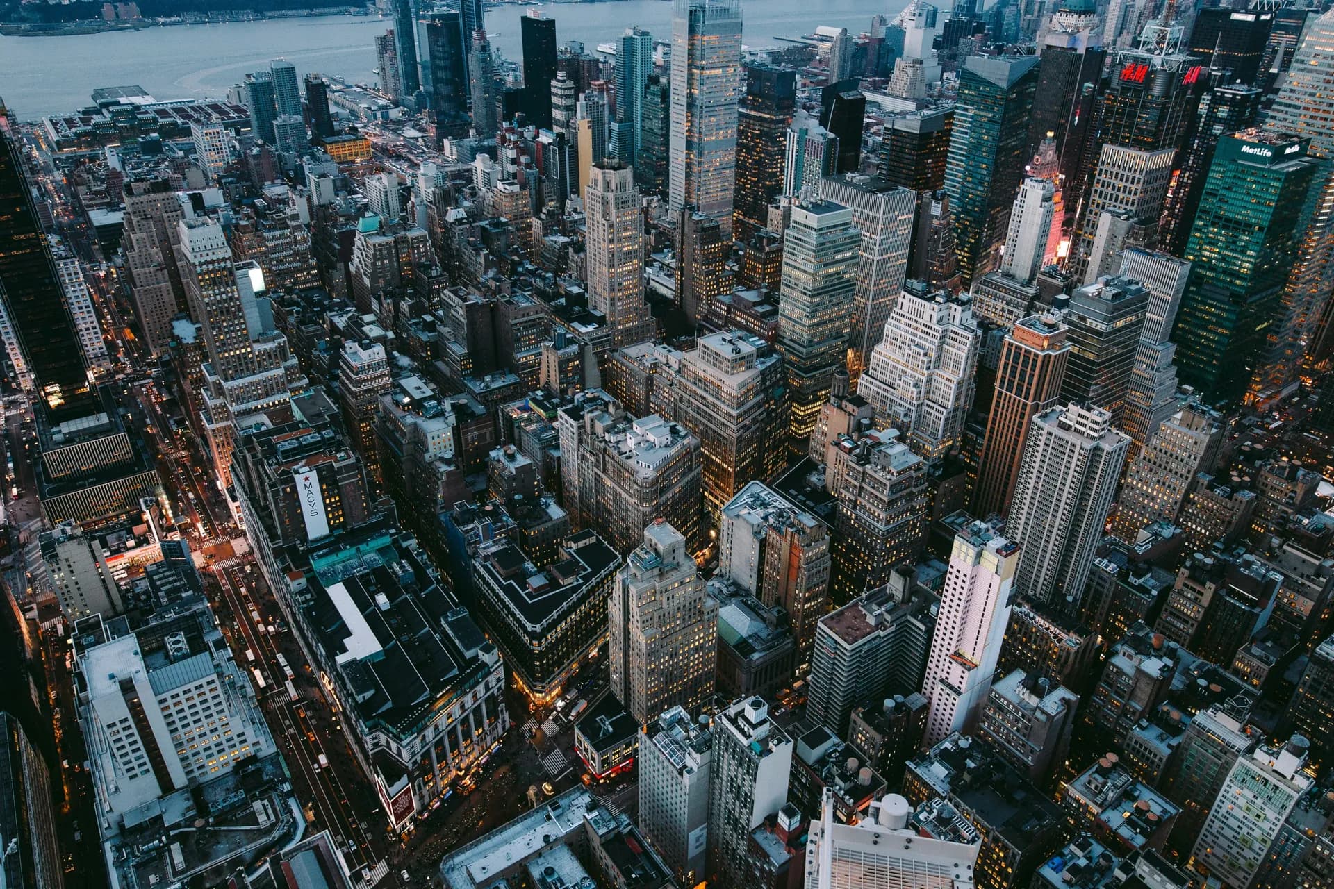 Aerial view of dense Manhattan skyscrapers and streets at dusk, with a river in the distance