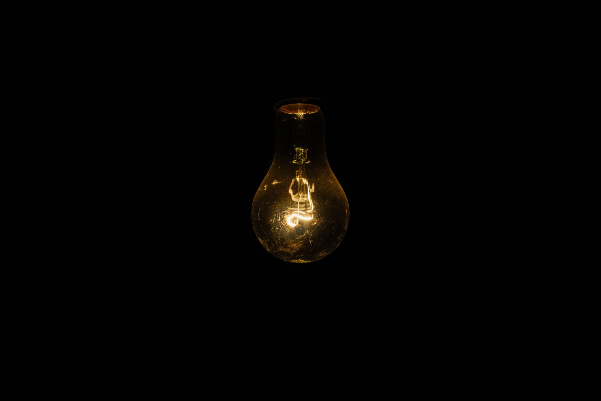A single dusty incandescent light bulb glowing faintly against a completely black background