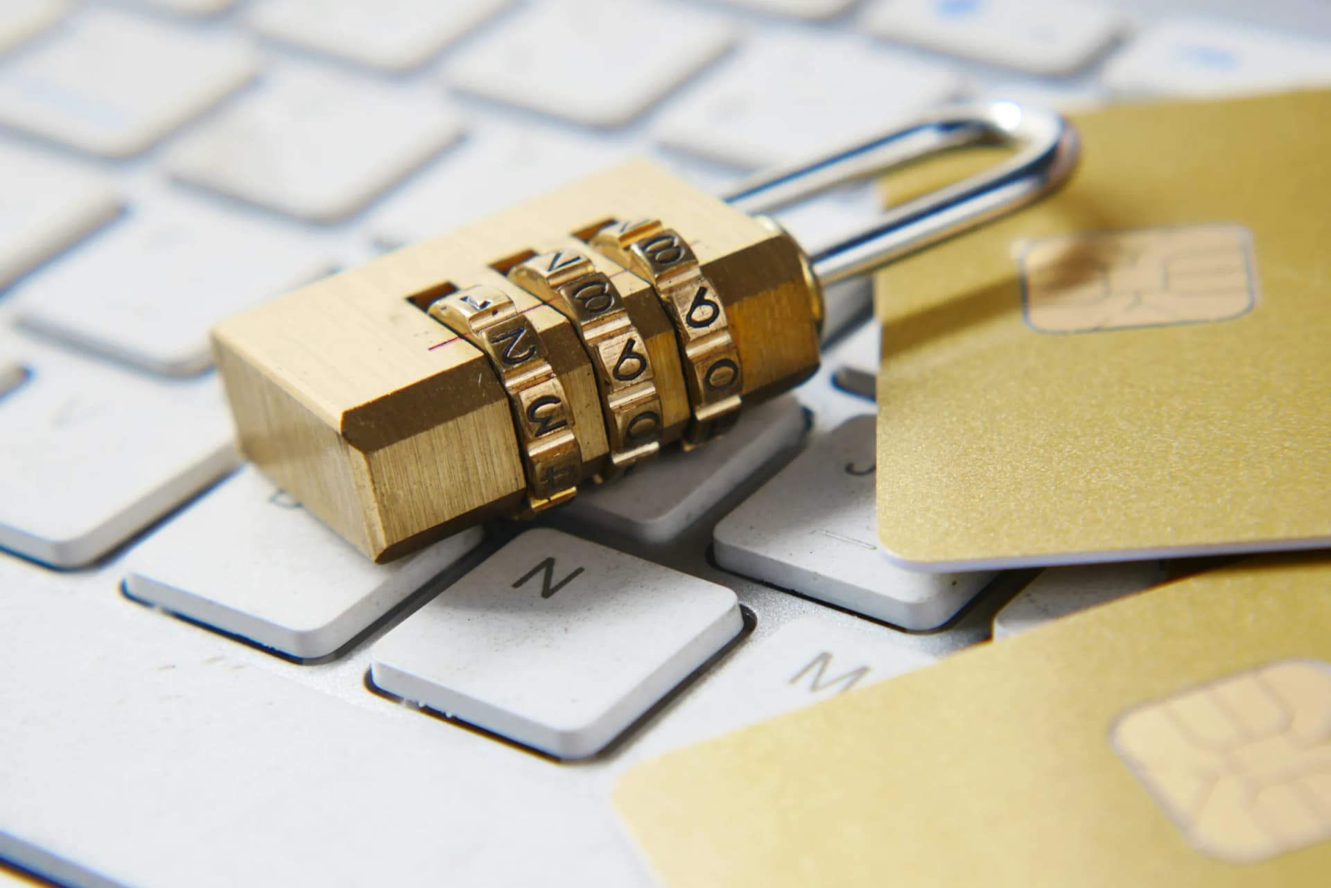 Brass combination padlock resting on a white keyboard next to two gold chip cards