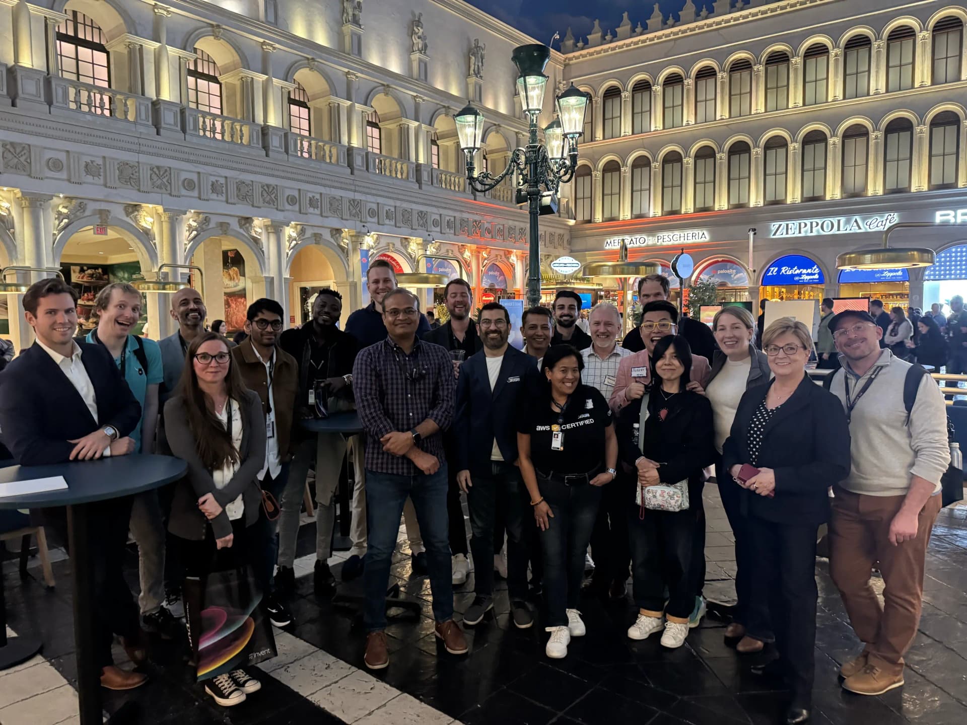 Group photo of about twenty Rearc team members at AWS re:Invent 2024, posing in a Venetian-style piazza with lamps and cafe storefronts